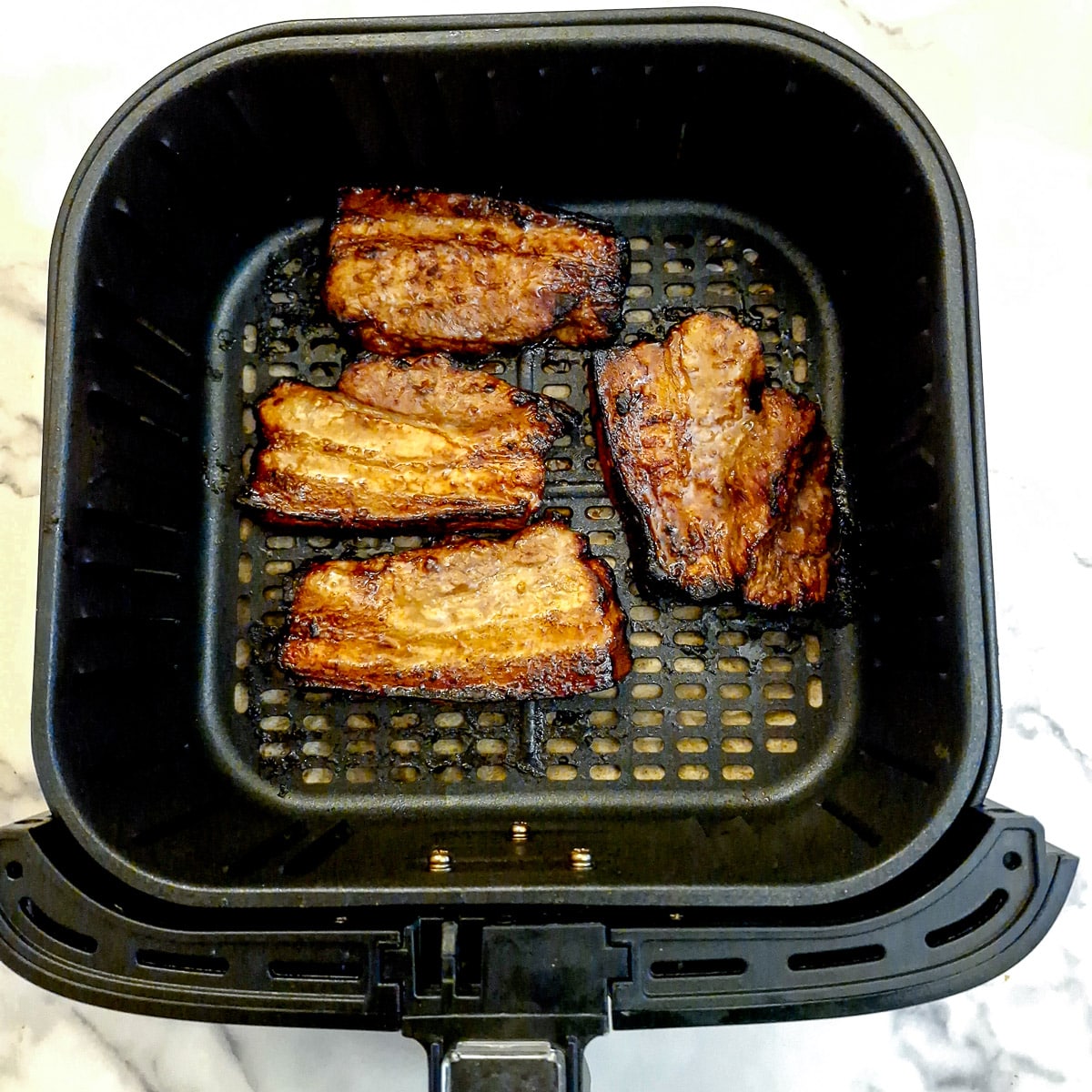 4 cooked pork belly slices in the basket of an air fryer.