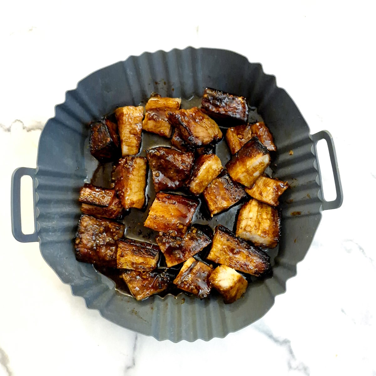 Pork belly cut into cubes and arranged in a silicone air fryer liner with the sauce.