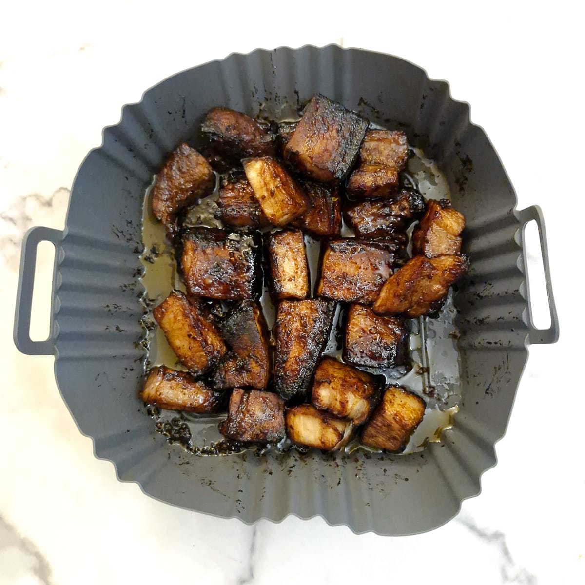 Cooked air fried pork belly bites in a silicone liner.