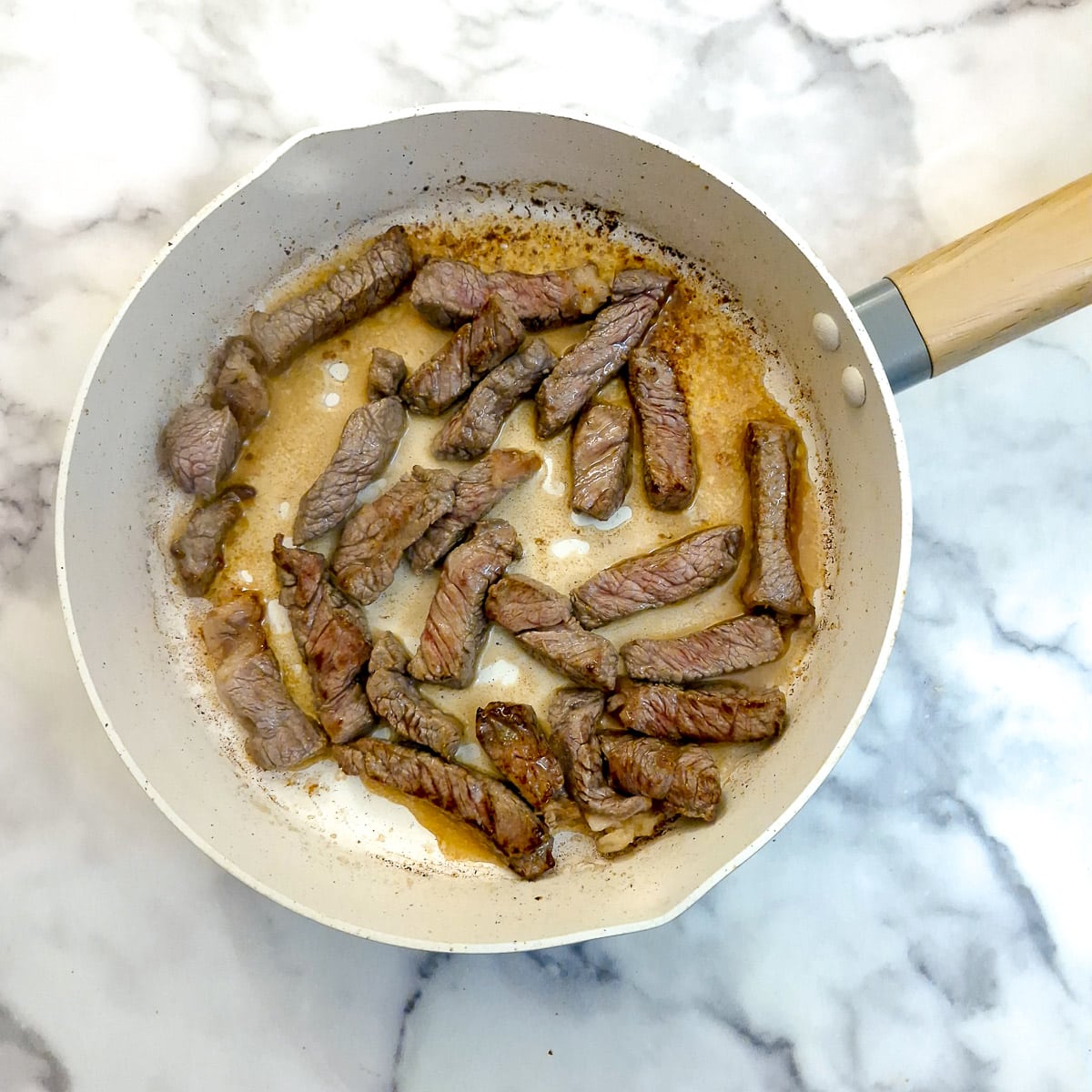 Strips of beef browning in a frying pan.