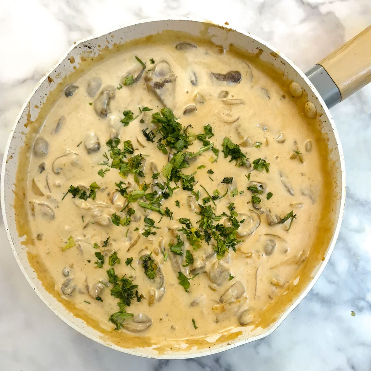 A frying pan with beef and mushroom stroganoff garnished with chopped parsley.