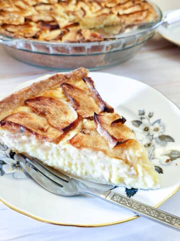 A slice of Canterbury apple tart on a blue patterned plate with a cake fork on the side.