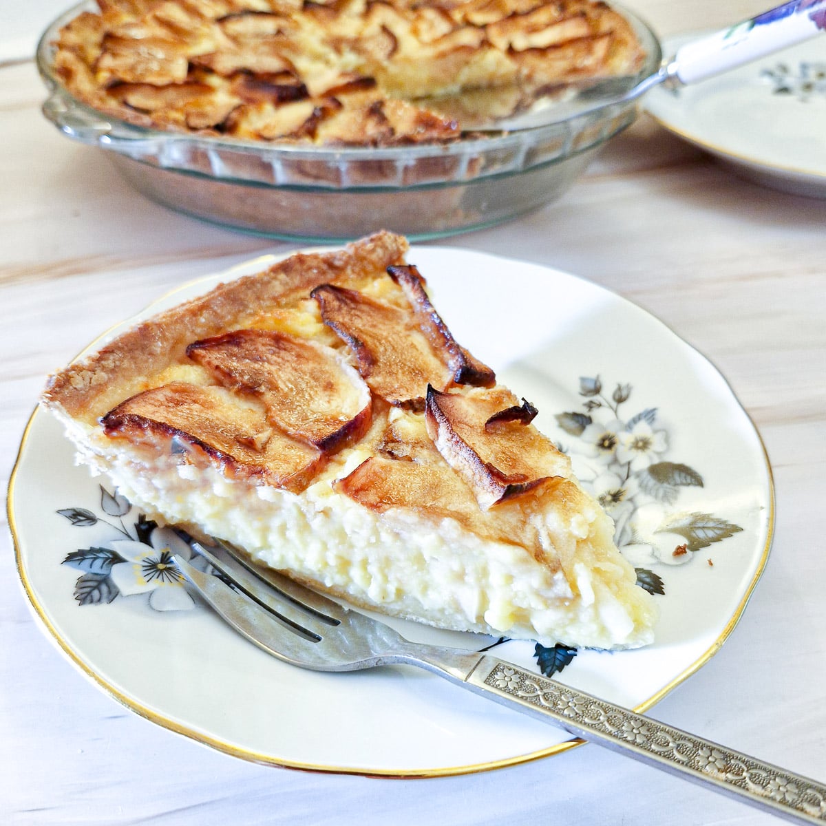 A slice of Canterbury apple tart on a blue patterned plate with a cake fork on the side.
