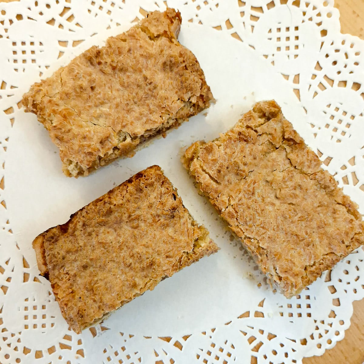 Three slices of coconut  jam slice on a white paper doily.