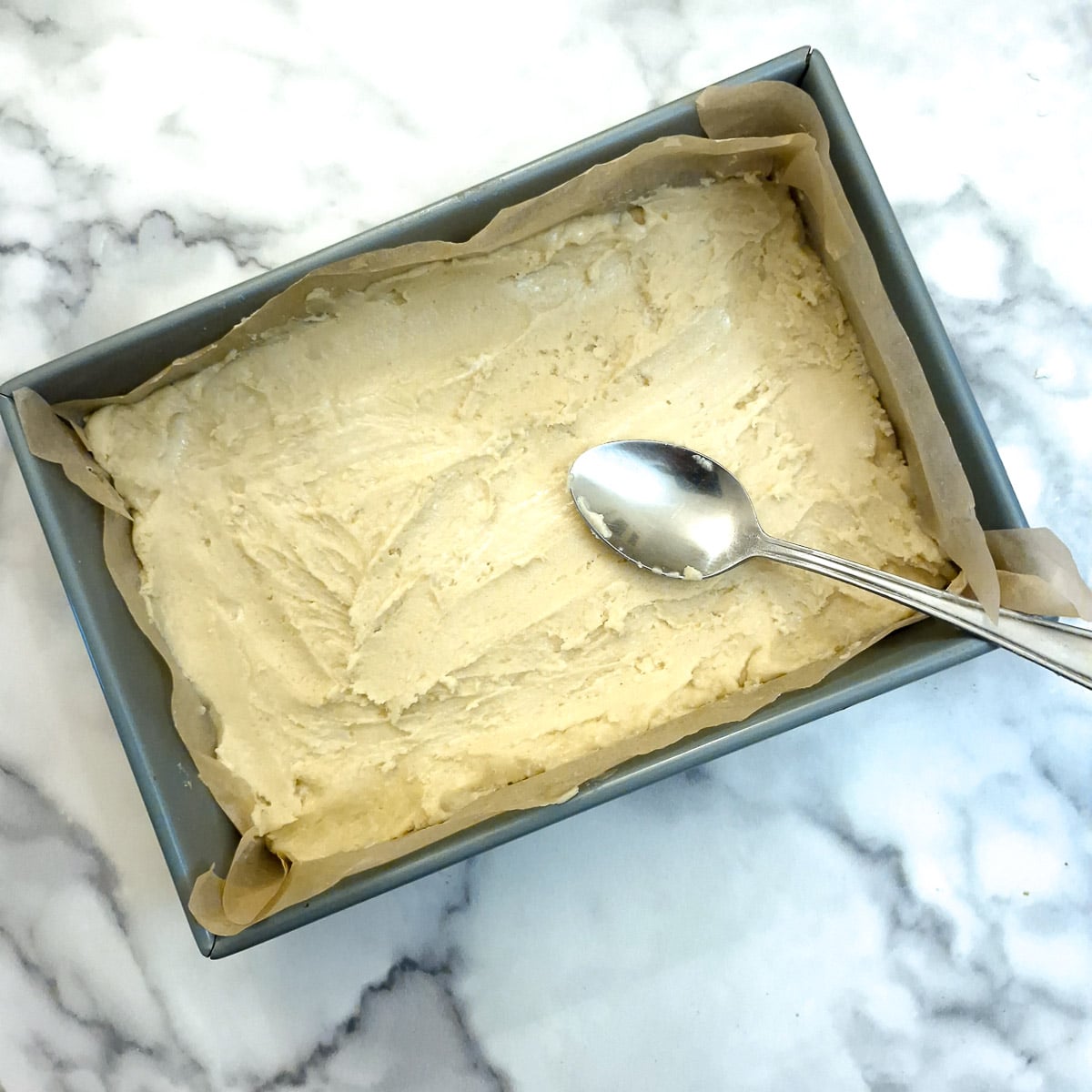 The sticky dough being spread into the baking dish with the help of a tablespoon.
