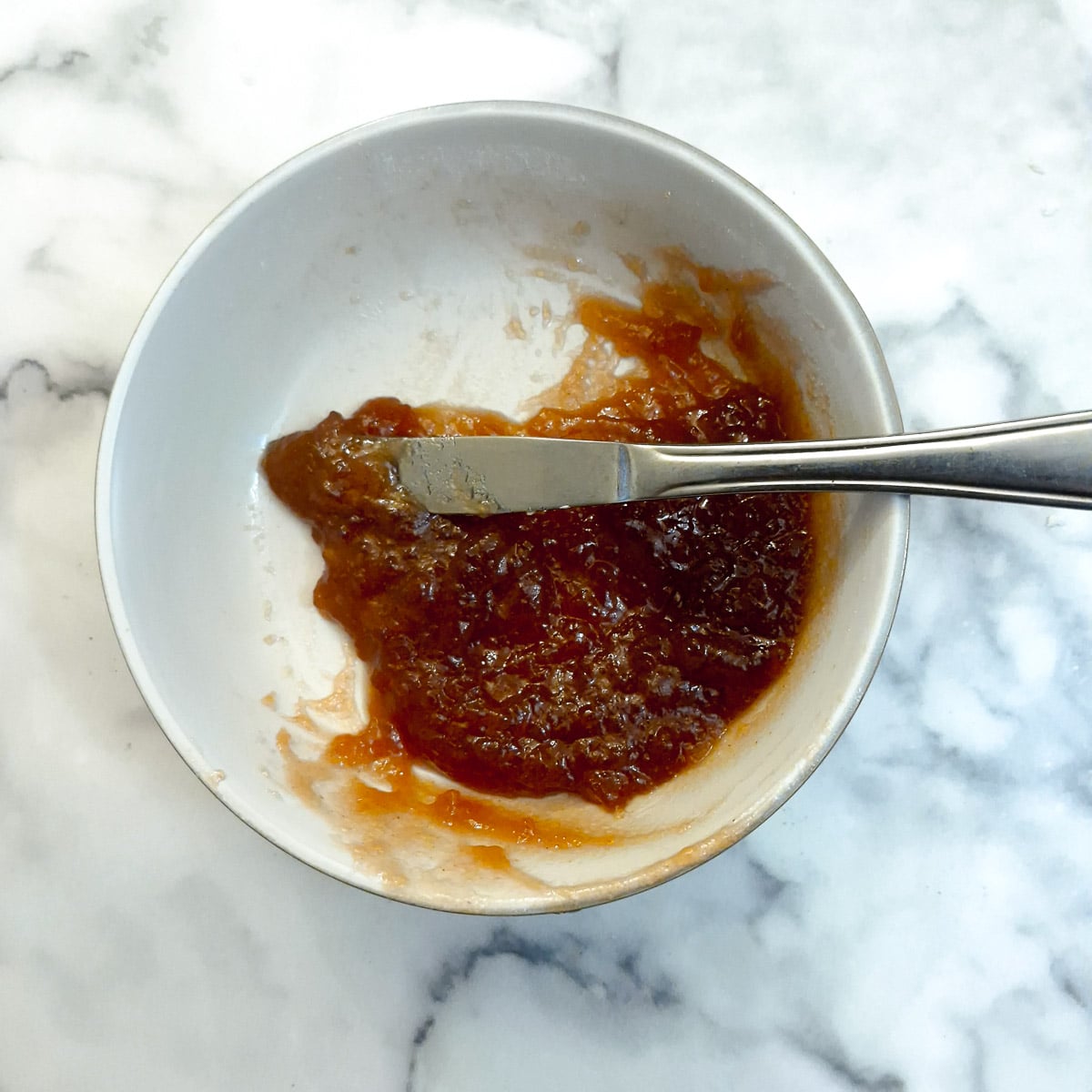 Strawberry jam being softened in a white bowl.