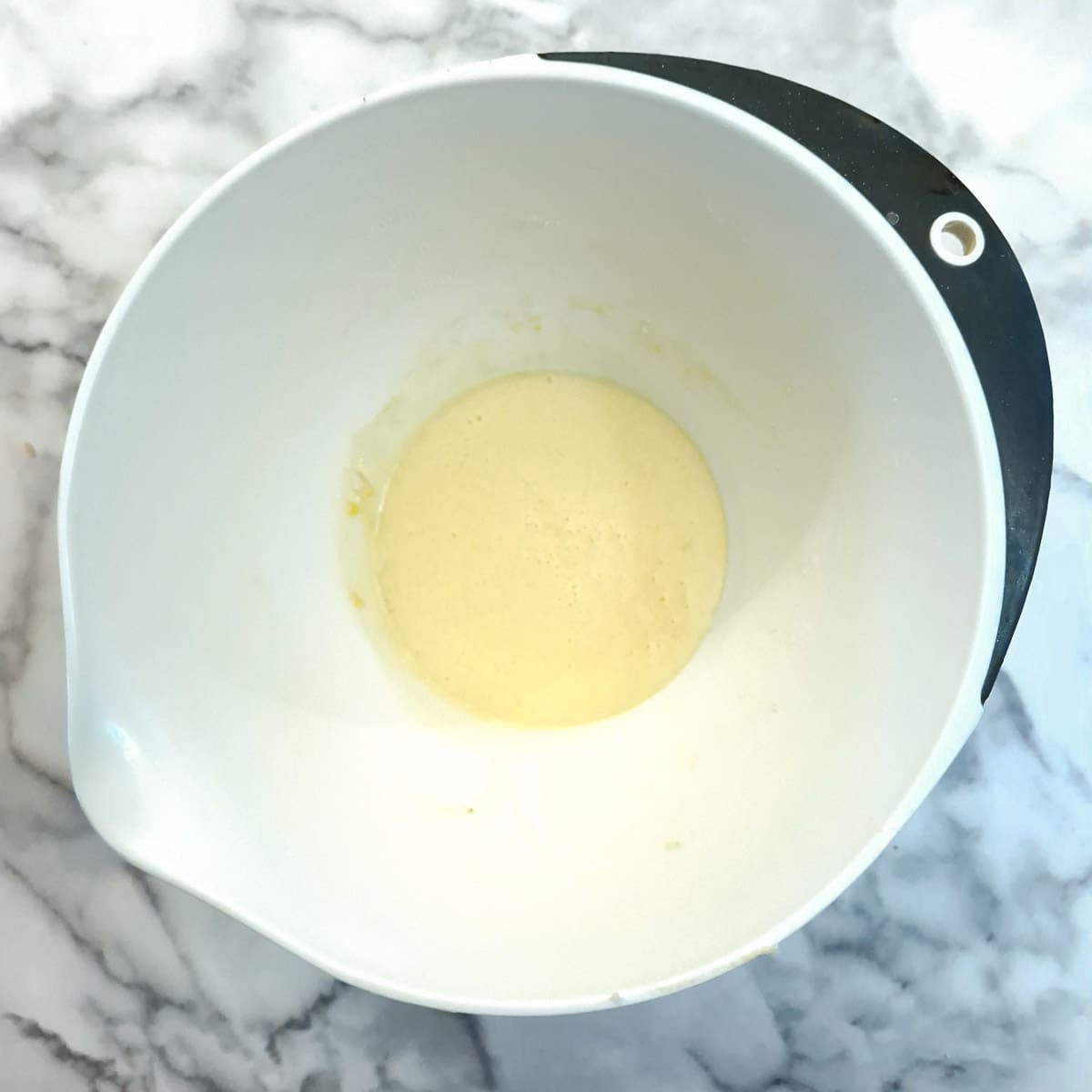 Eggs and sugar whisked together in a white mixing bowl.