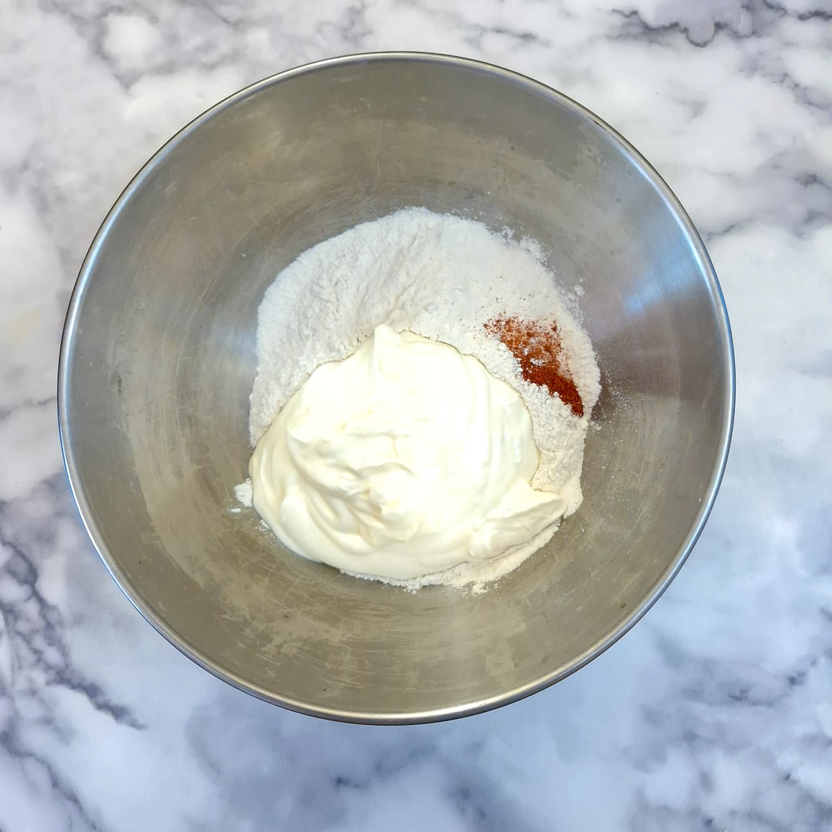 Flour, yoghurt and paprika in a metal mixing bowl.