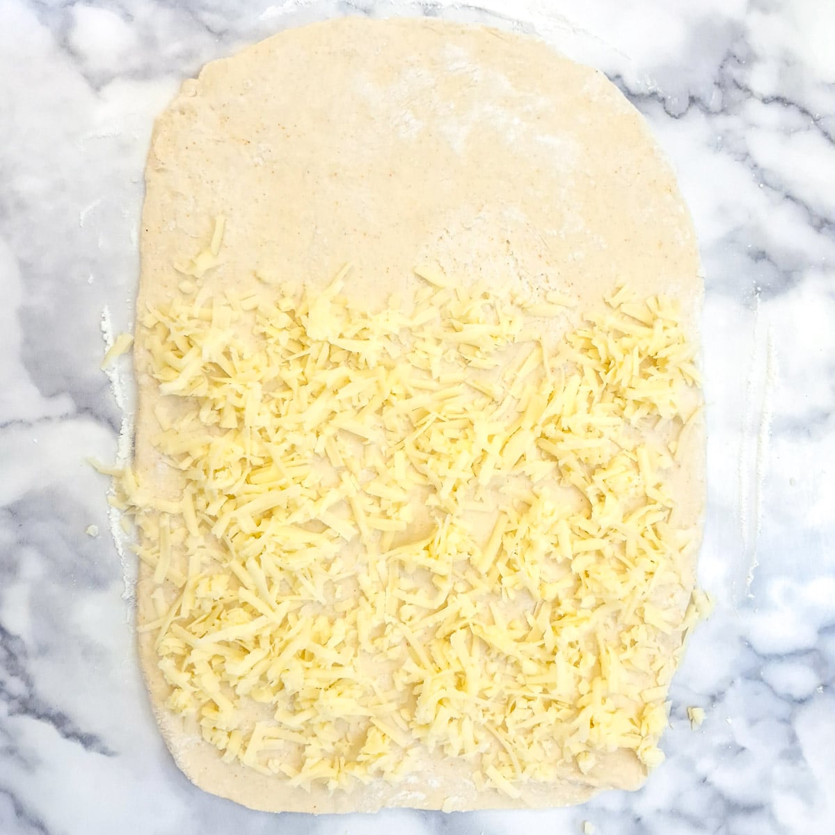 A rectangle of pastry with two thirds covered in grated cheese.