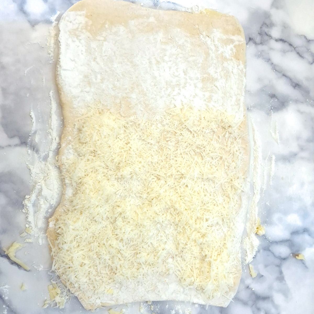 A rectangle of pastry with two thirds covered in grated parmesan cheese.