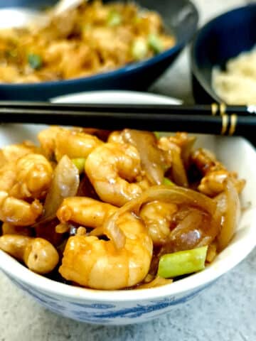 A shall bowl filled with kung pao prawns with a pair of chopsticks balanced on top.