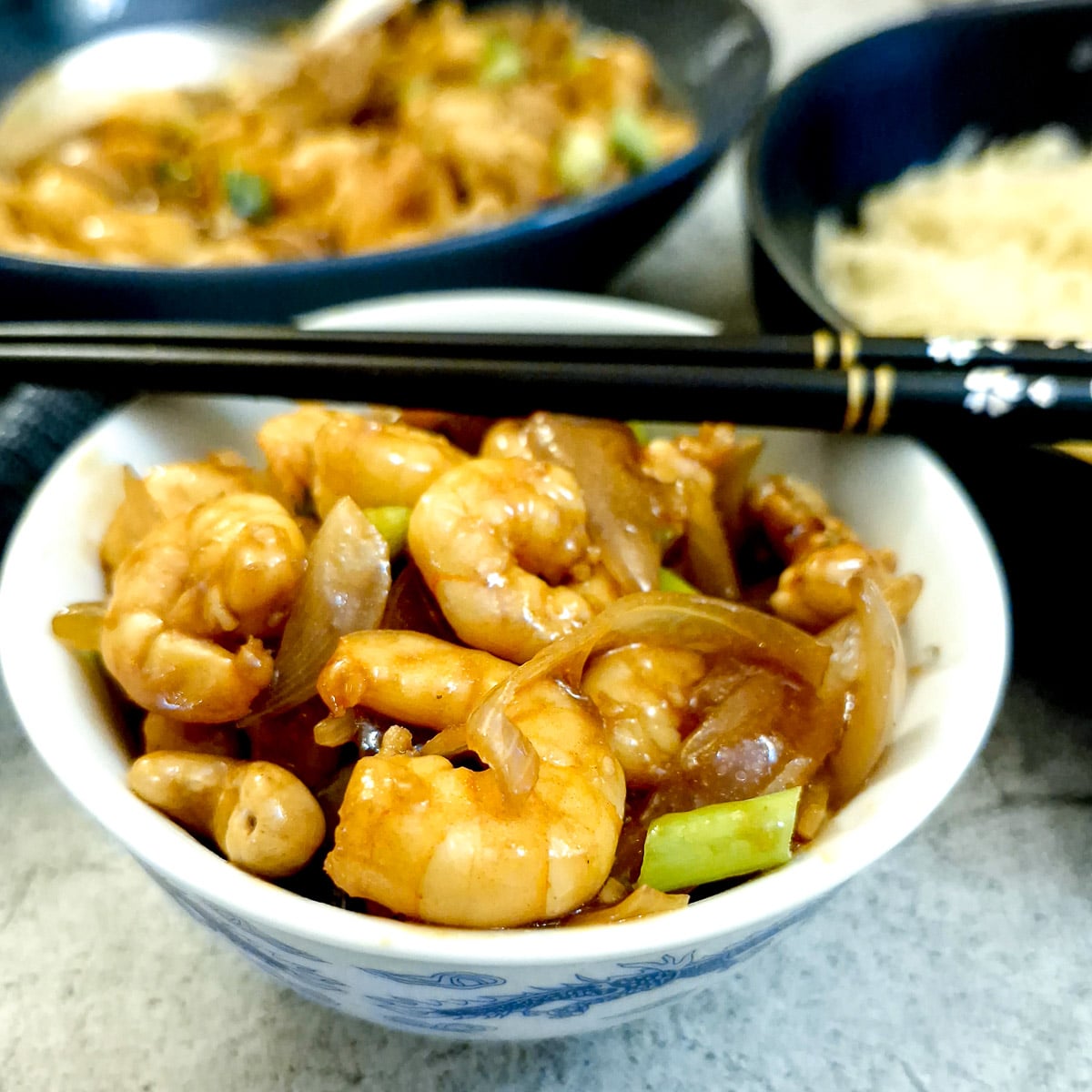 A shall bowl filled with kung pao prawns with a pair of chopsticks balanced on top.