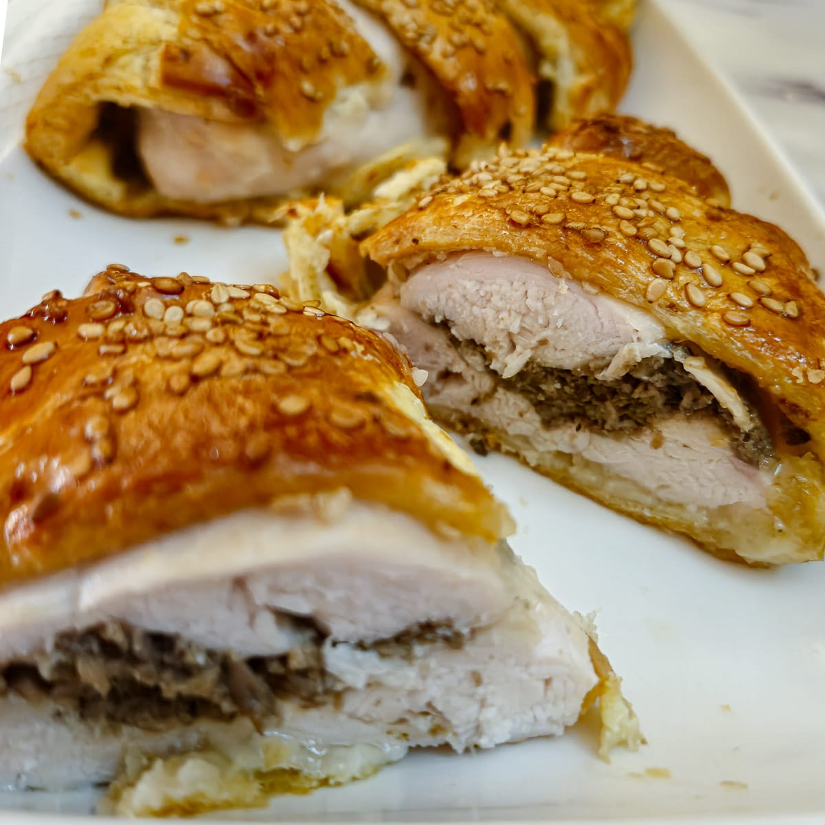 Slices of mushroom-stuffed chicken en croute on a white plate.