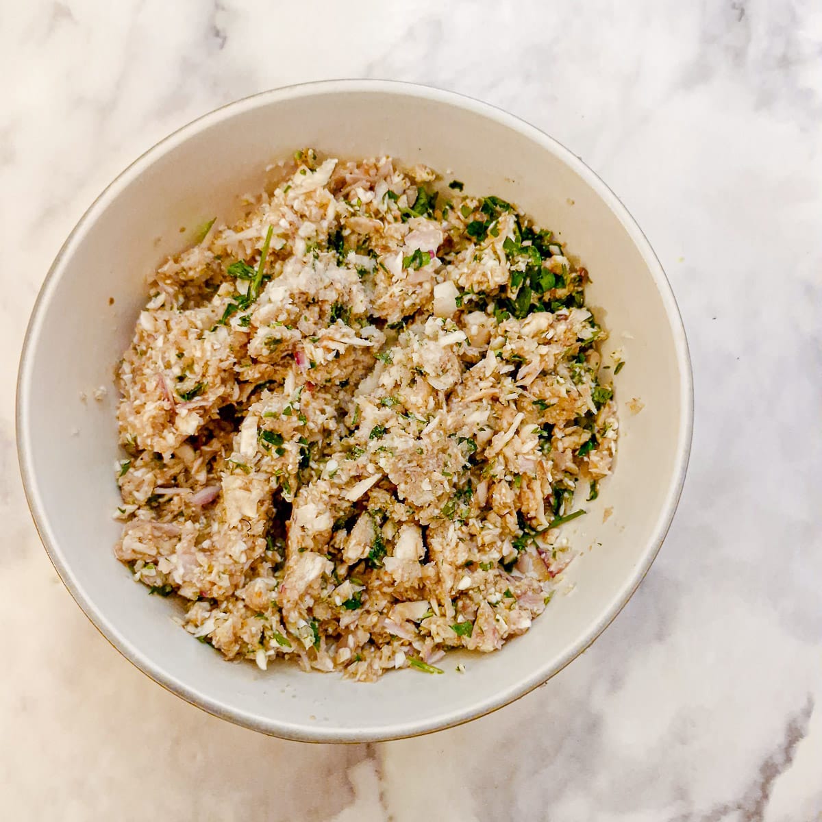 Finely chopped mushrooms, shallots and herbs in a white bowl.