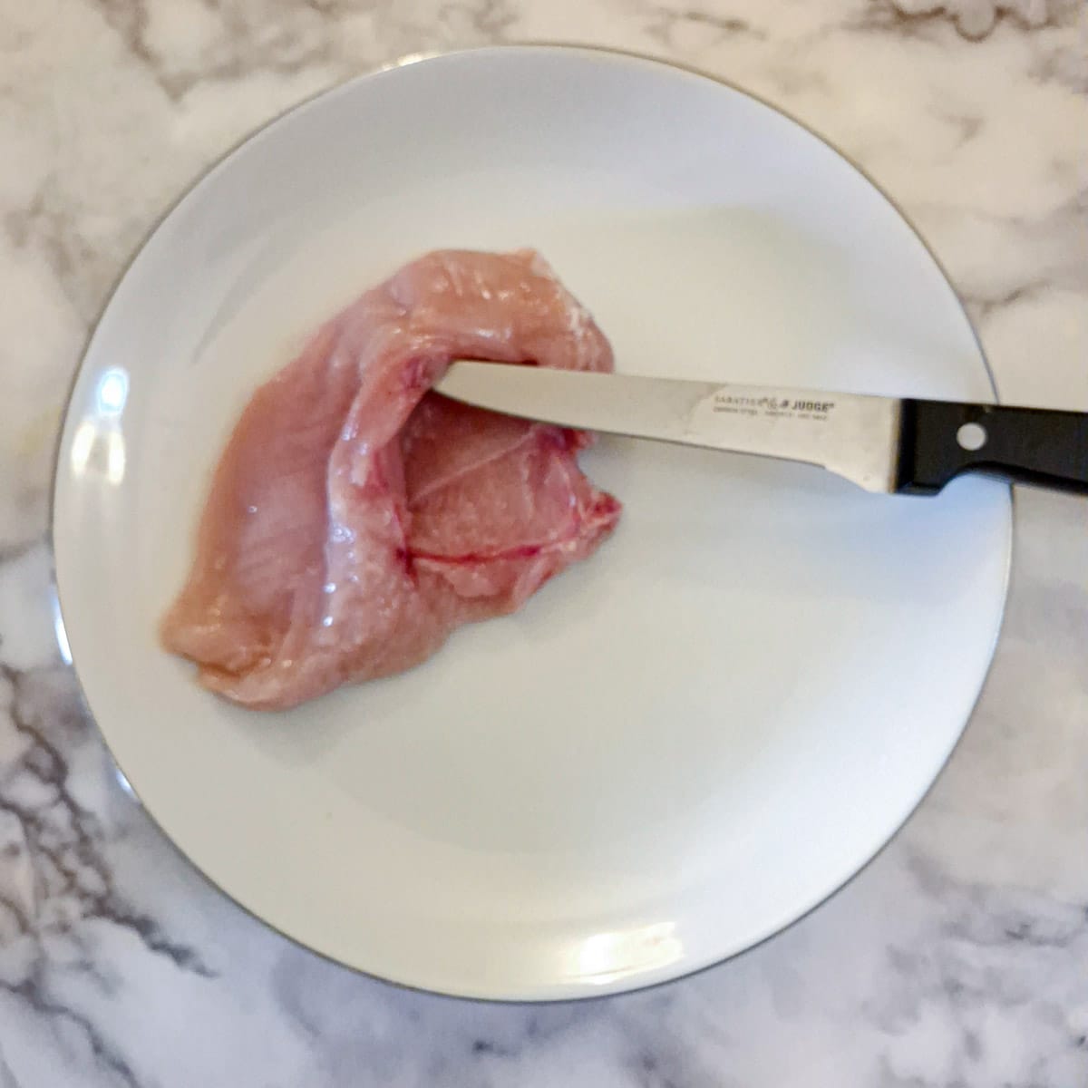 A pocket being cut into a chicken breast with a sharp knife.