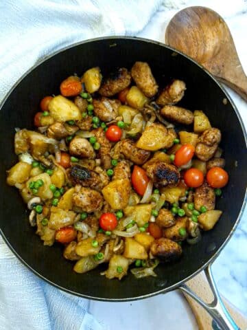 A pan of sausage and potato hash alongside a wooden serving spoon.