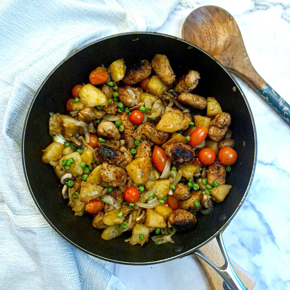 A pan of sausage and potato hash alongside a wooden serving spoon.