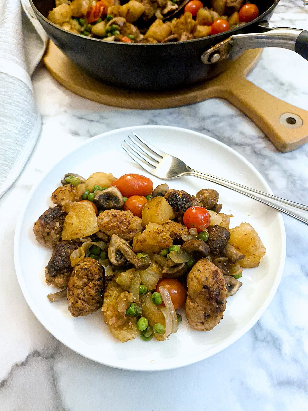 Sausage and potato hash on a white plate with a fork.