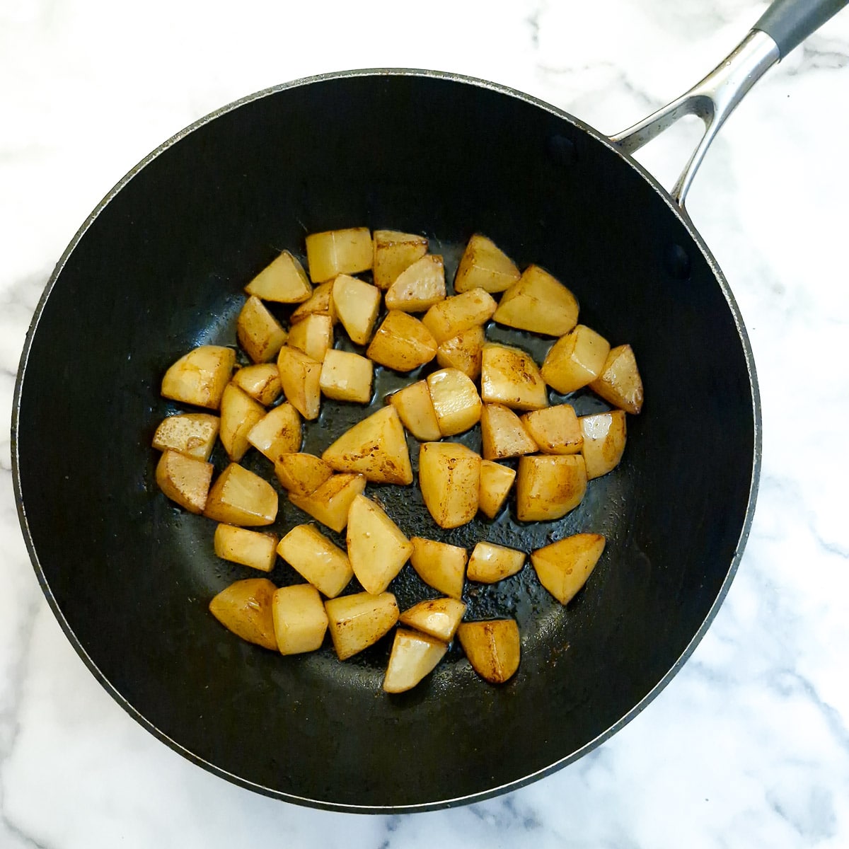 Browned cubed potatoes in a frying pan.