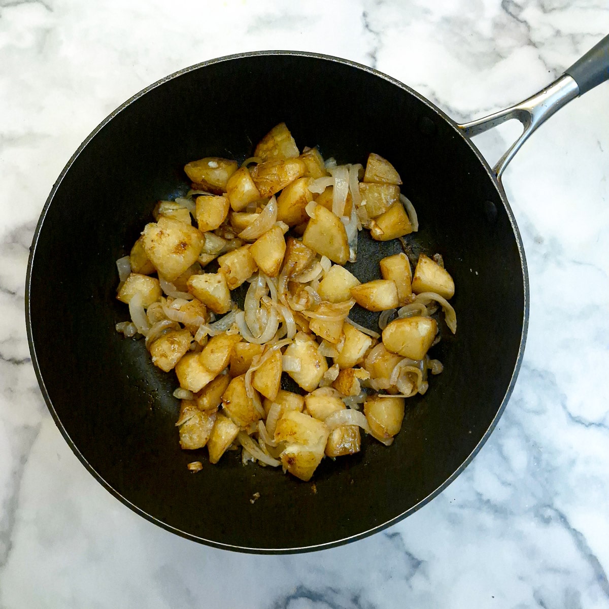 Browned potatoes and onions in a frying pan.