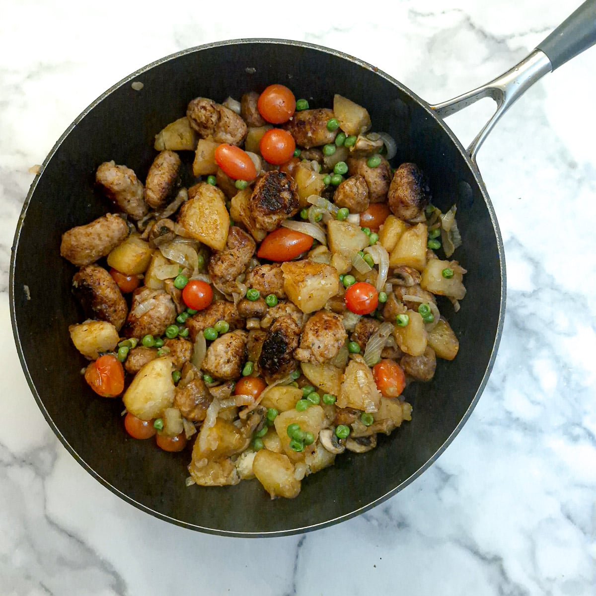 Cooked sausage and potato hash in a frying pan.