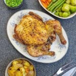 An air fryer roast chicken on a serving plate surrounded by dishes of vegetables.