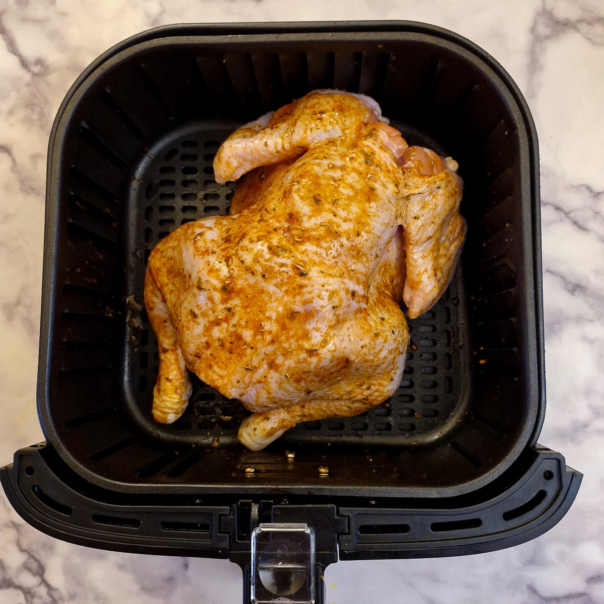 A whole chicken placed breast-side down in an air fryer basket.