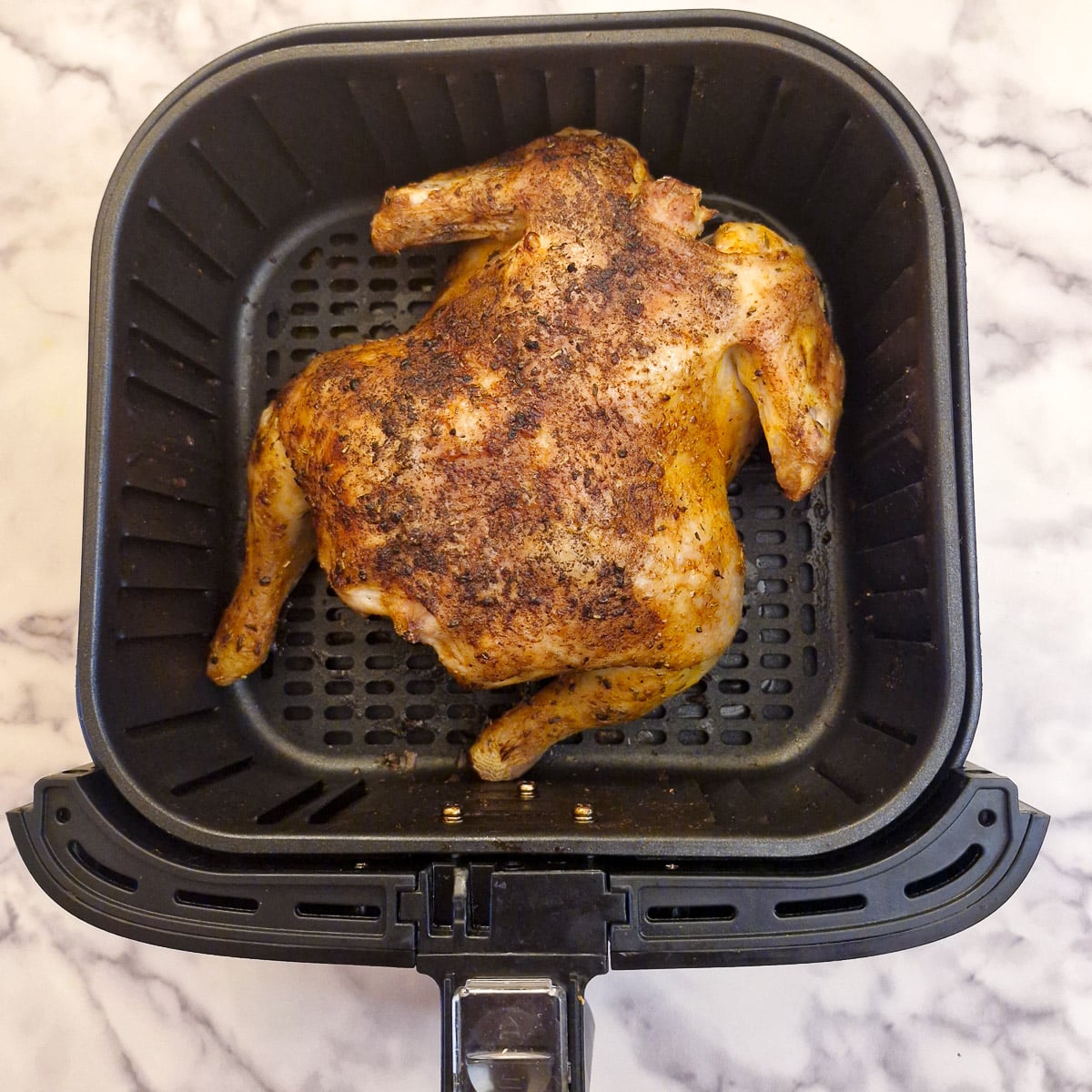 A whole chicken after being cooked for 40 minutes in an air fryer basket.