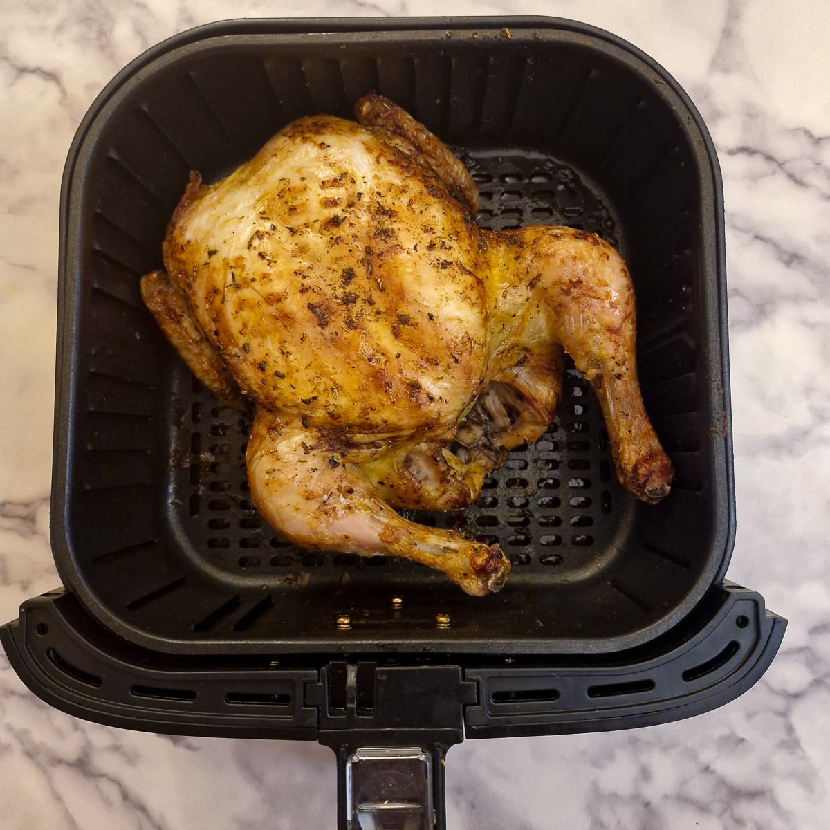 A whole cooked chicken in an air-fryer basket.