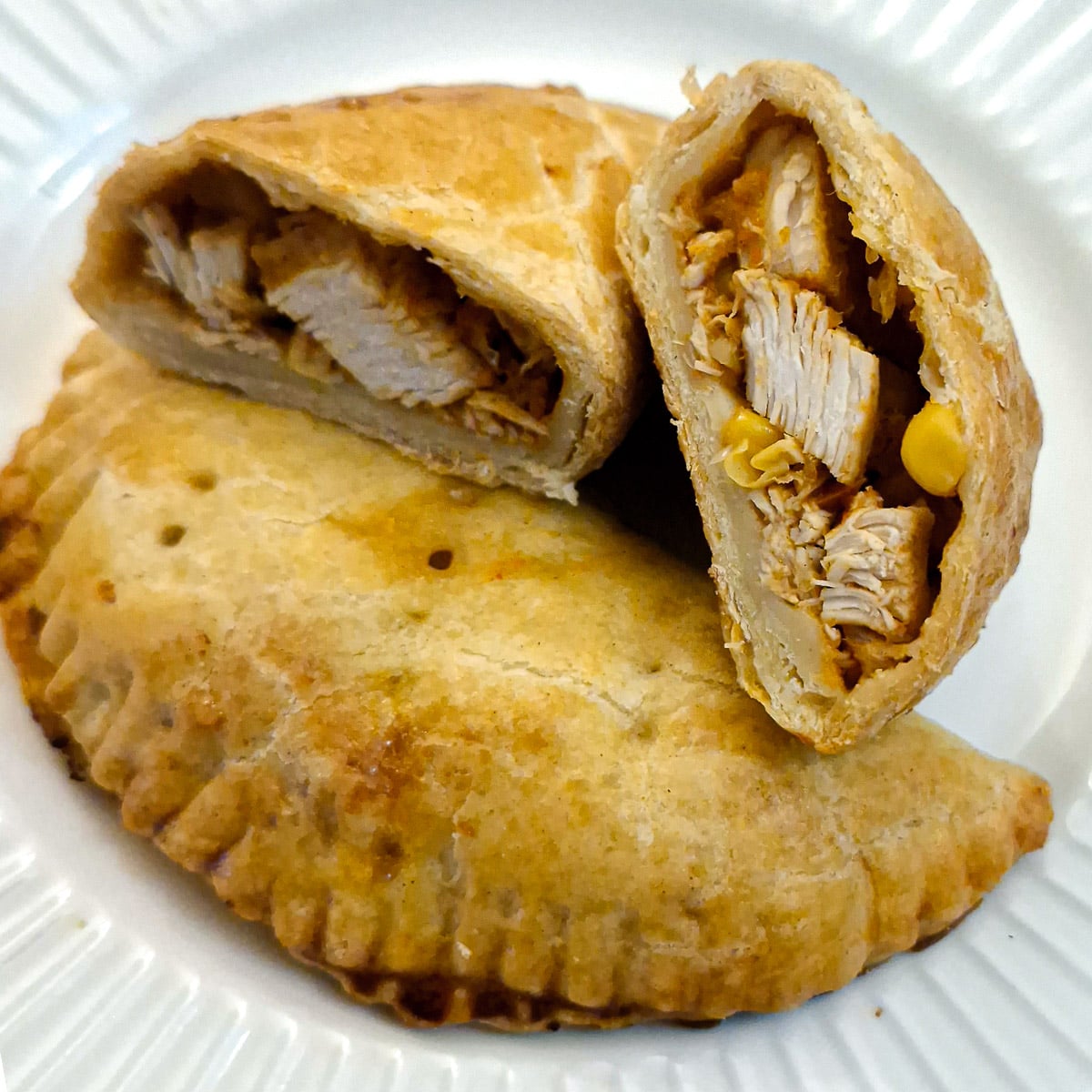 Two halves of a chicken empanada showing the filling inside.