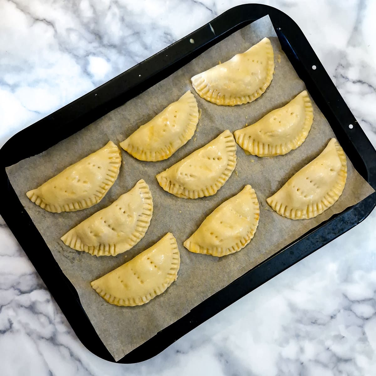 9 unbaked chicken empanadas on a baking tray.