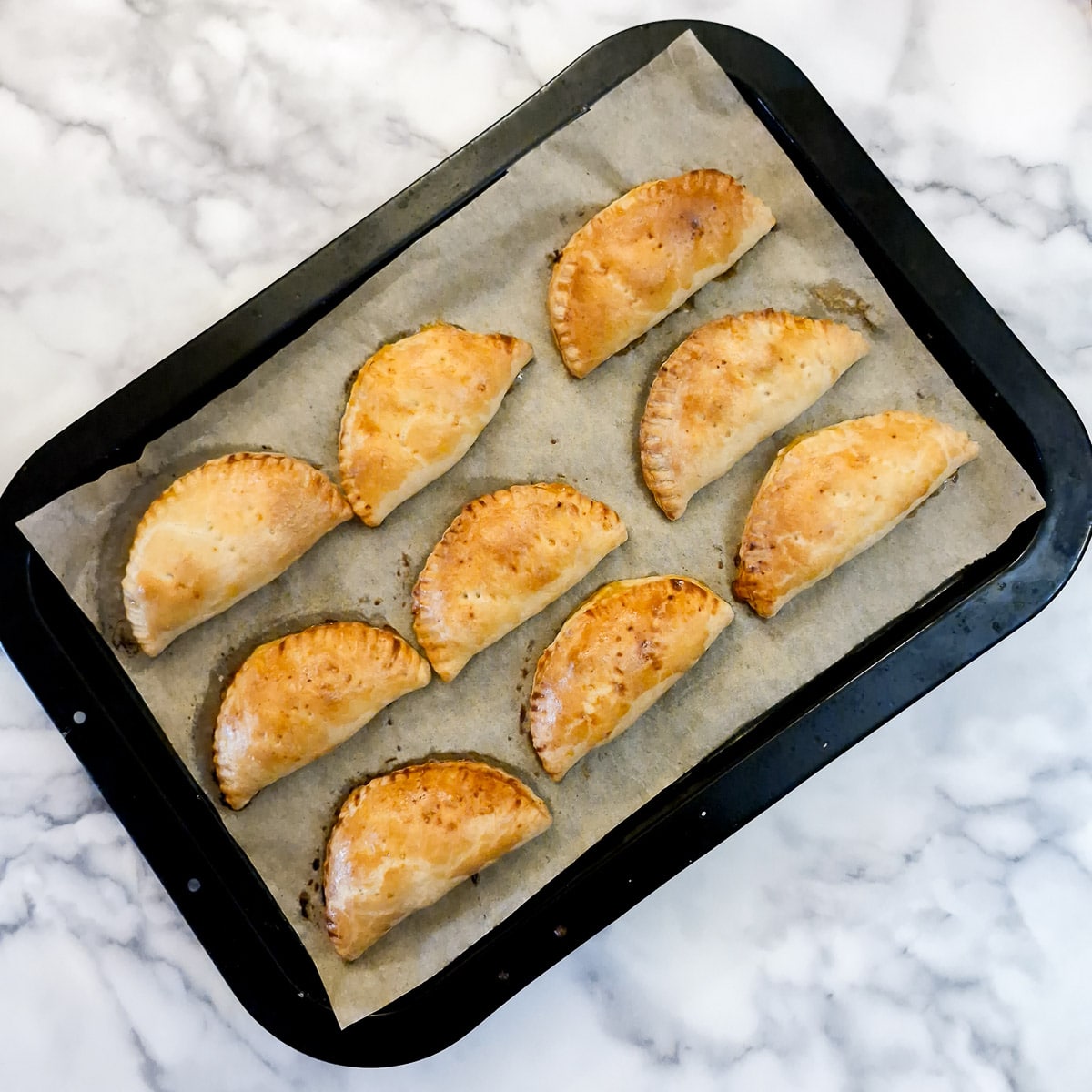 9 golden brown baked chicken empanadas on a baking tray.