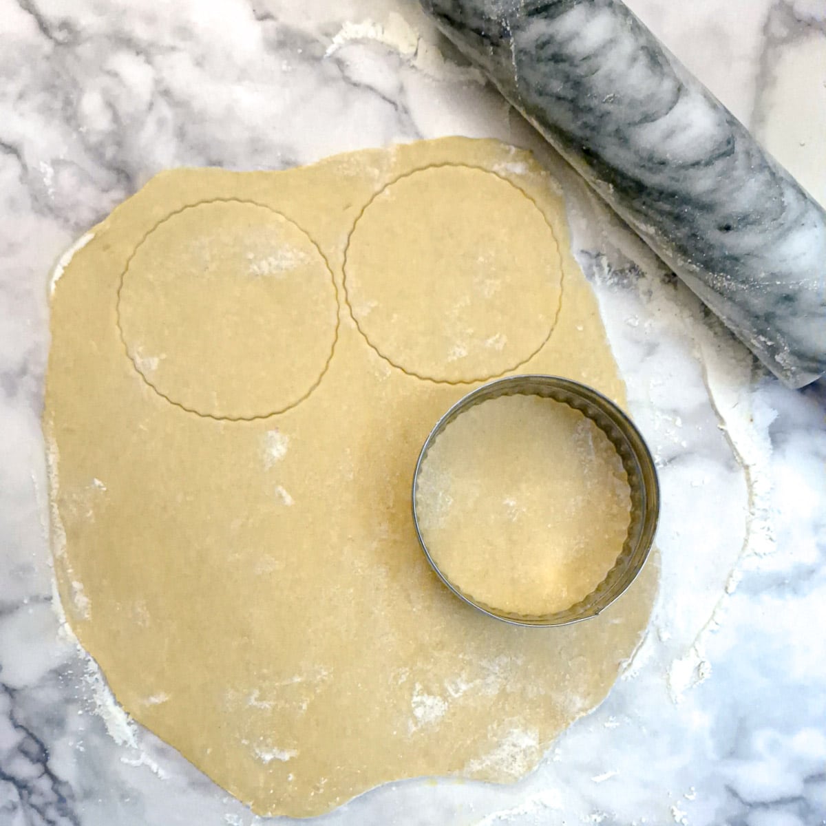 Rolled out pastry being cut into circles with a scone cutter.