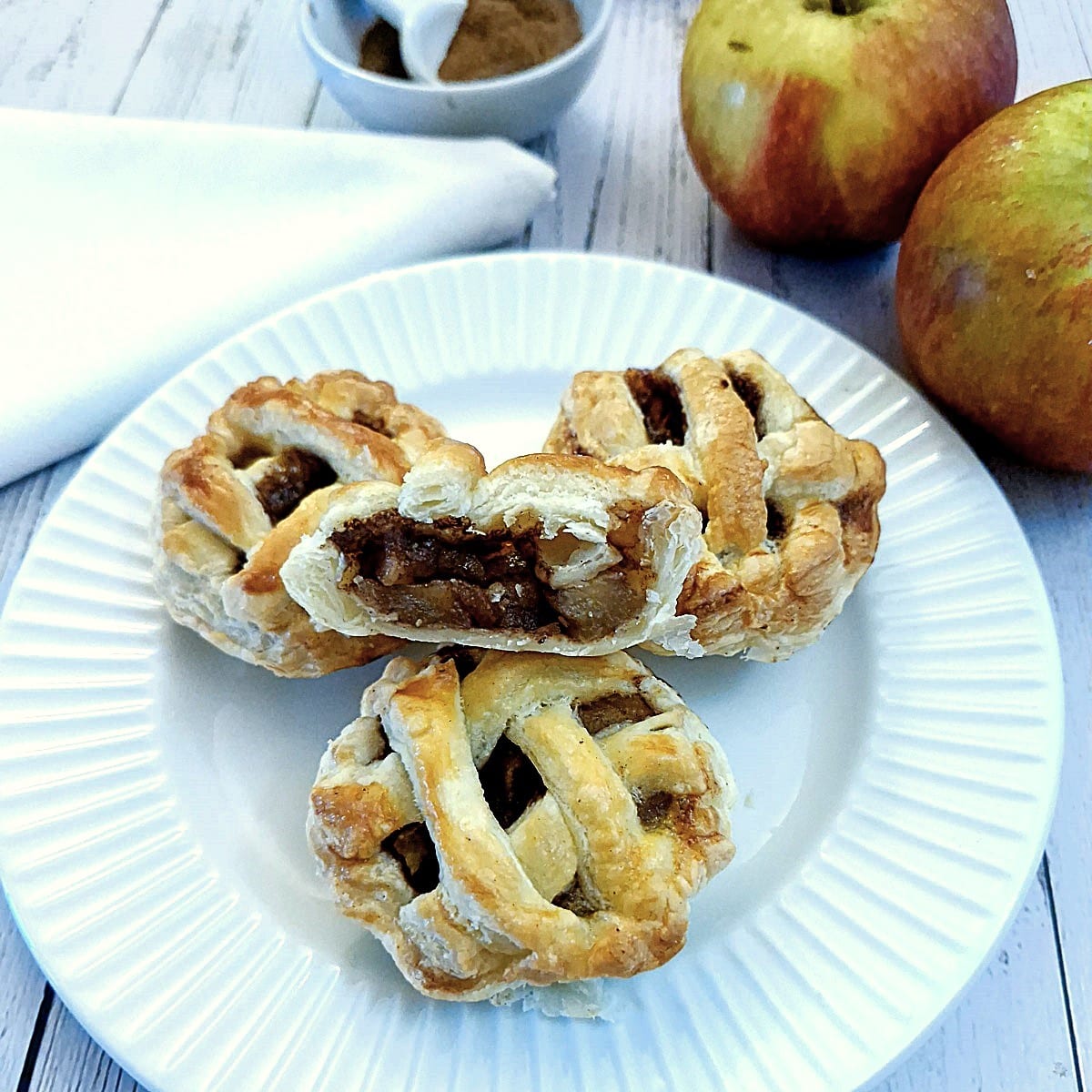 Three caramel apple pies on a plate with one cut open to show the inside.