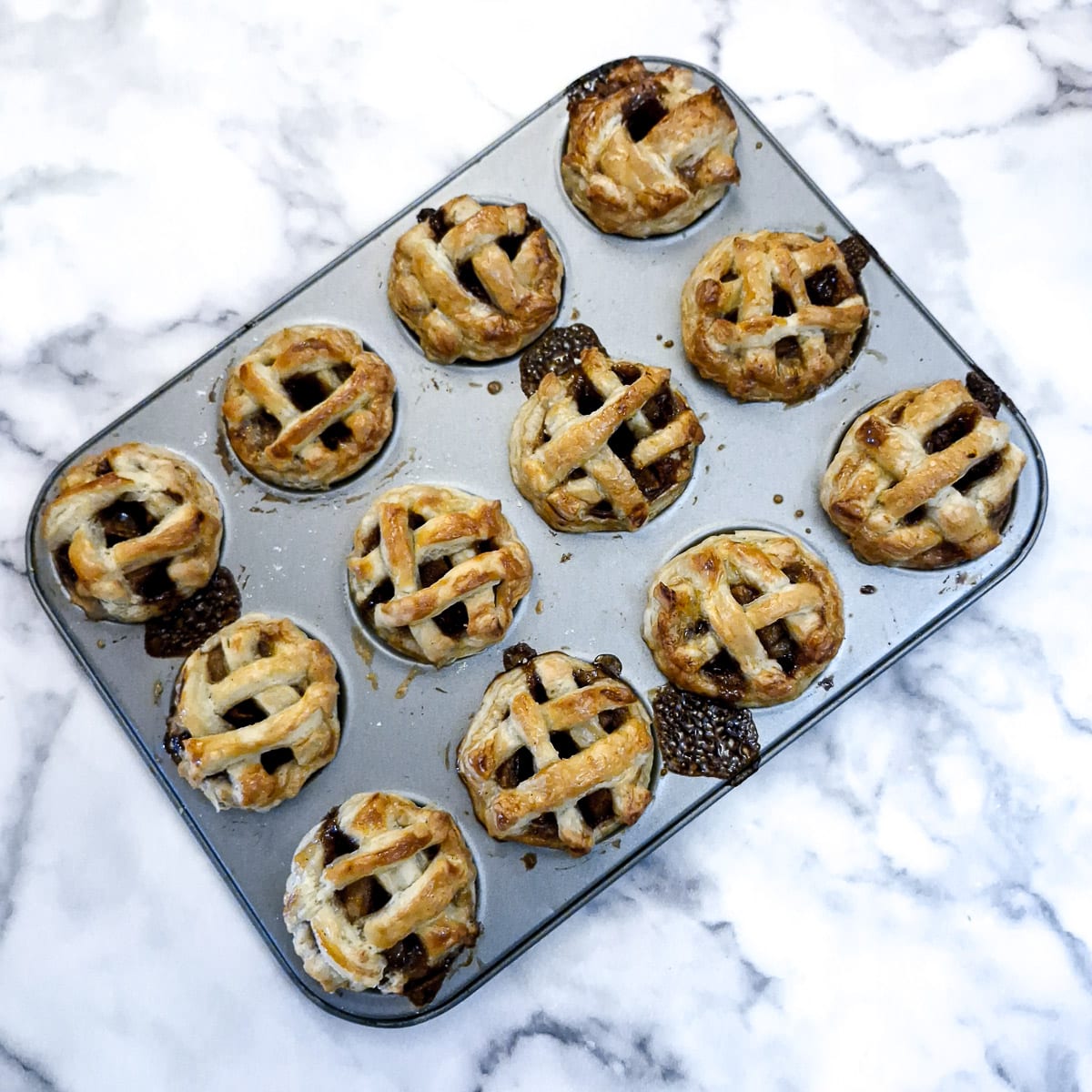 12 baked mini apple pies  in a baking tin.