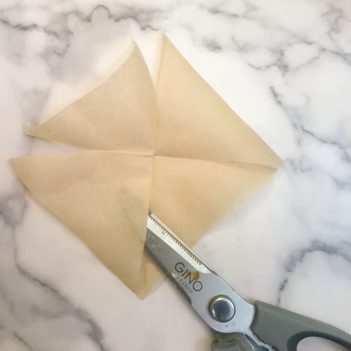 Parchment paper being cut diagonally on each corner so it fits easily into a muffin tin.