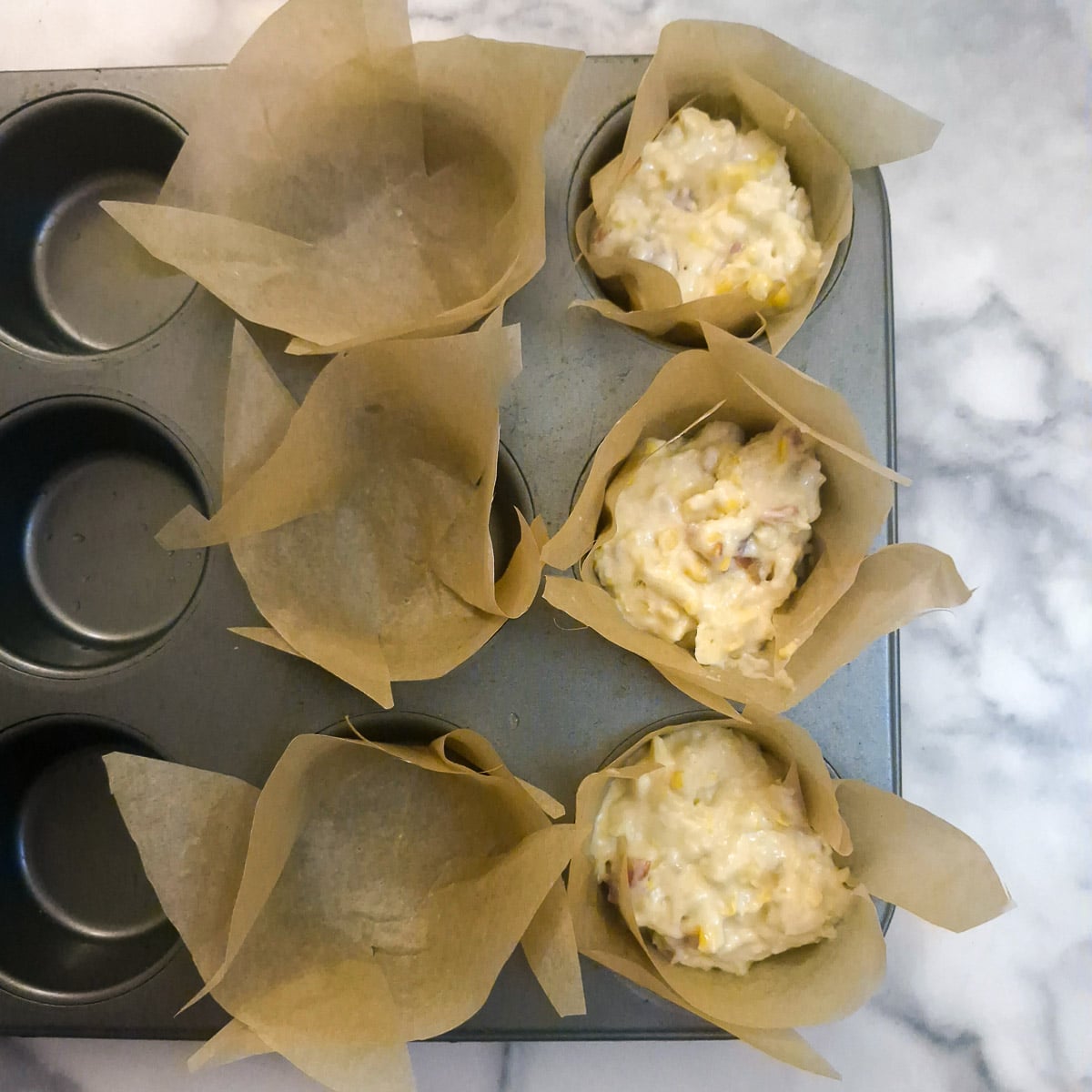 Cornbread batter being spooned into lined muffin tins.
