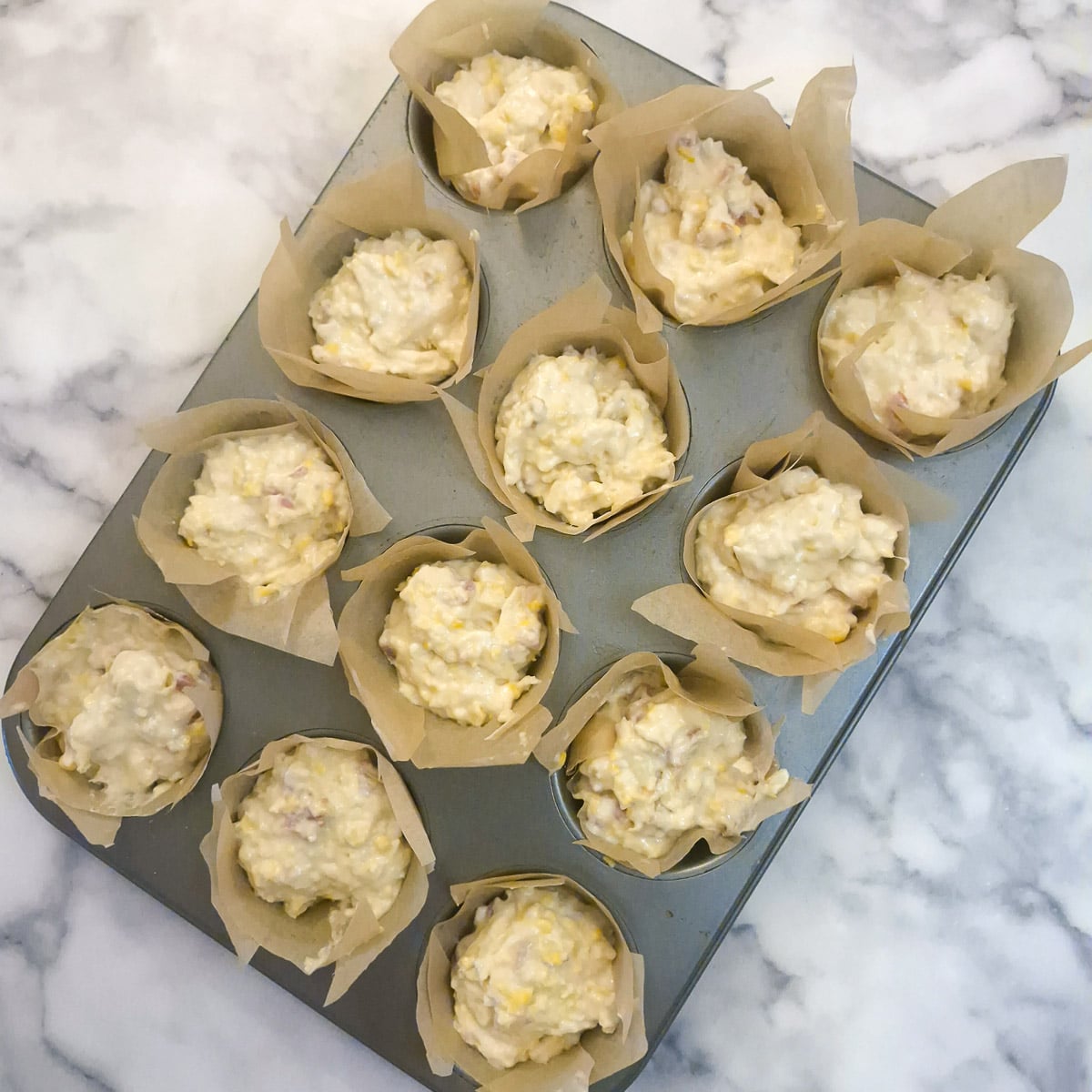 12 unbaked cornbread muffins in a baking tin.