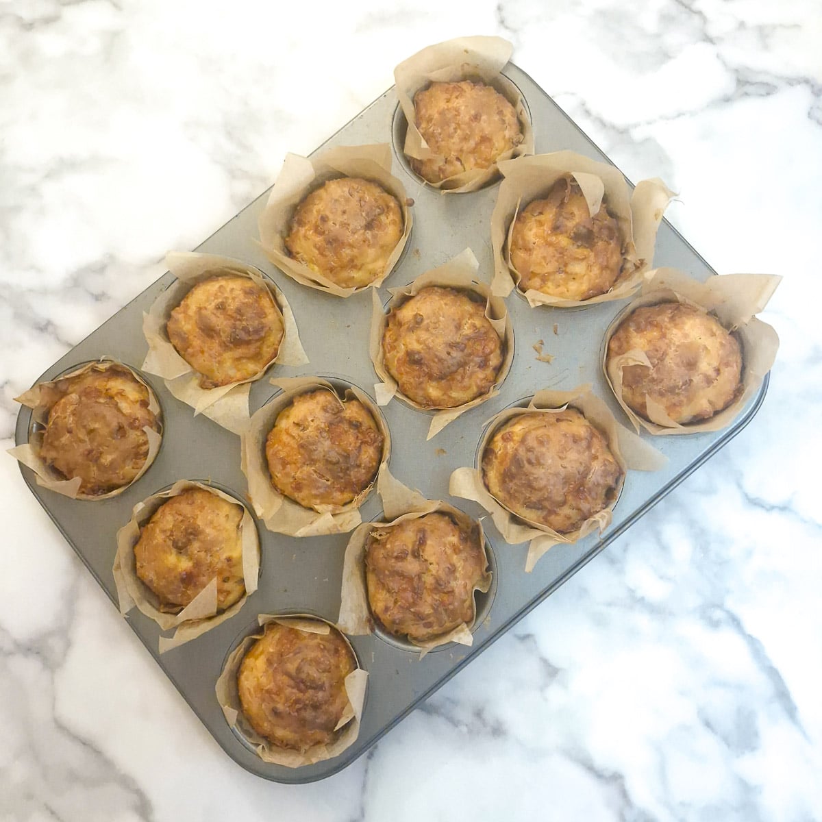12 baked cornbread muffins in a baking tin.