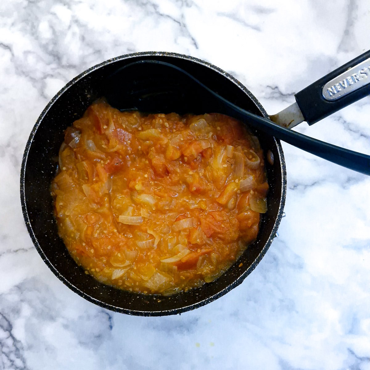 Cooked tomato and onion gravy in a saucepan.