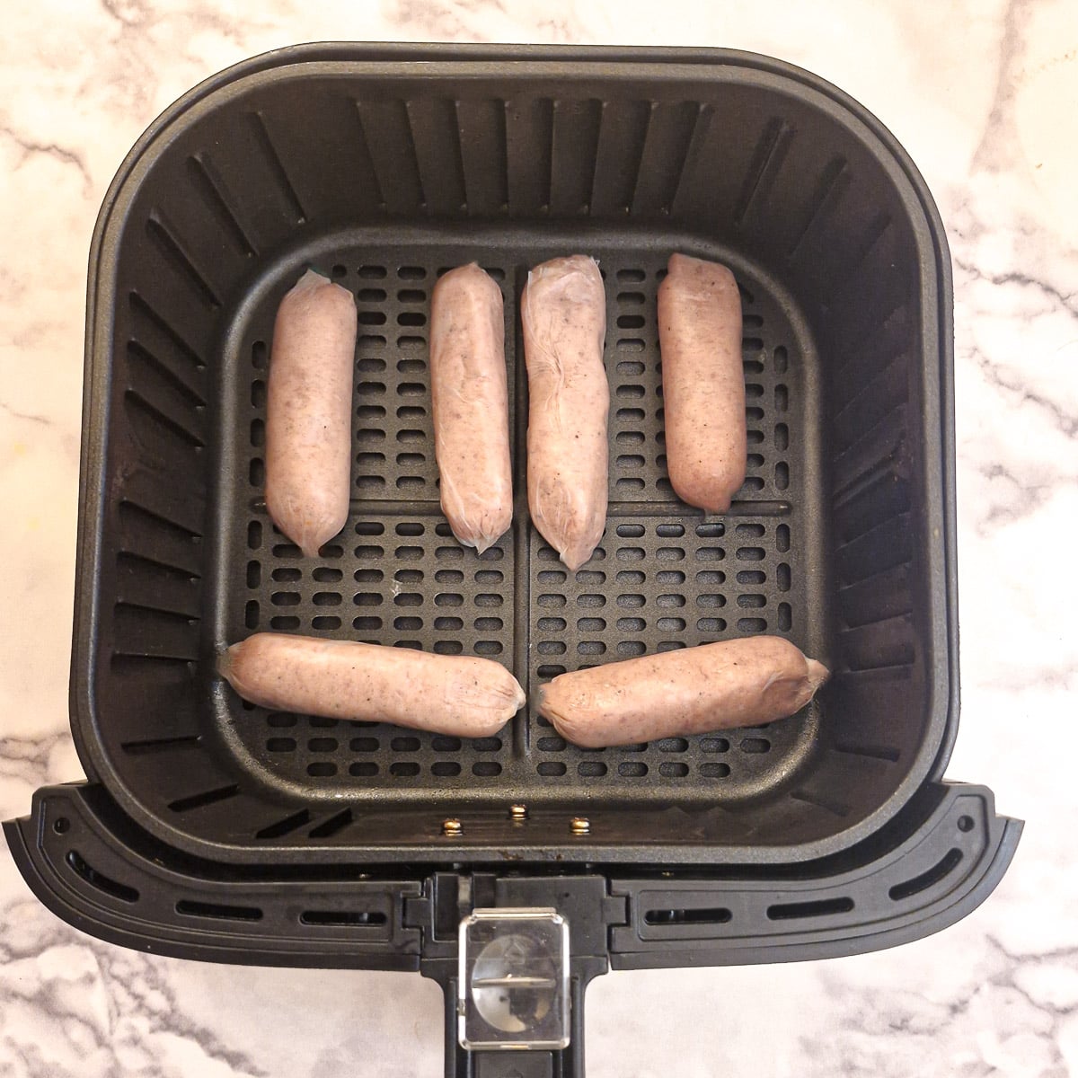 6 raw sausages in an air fryer basket.