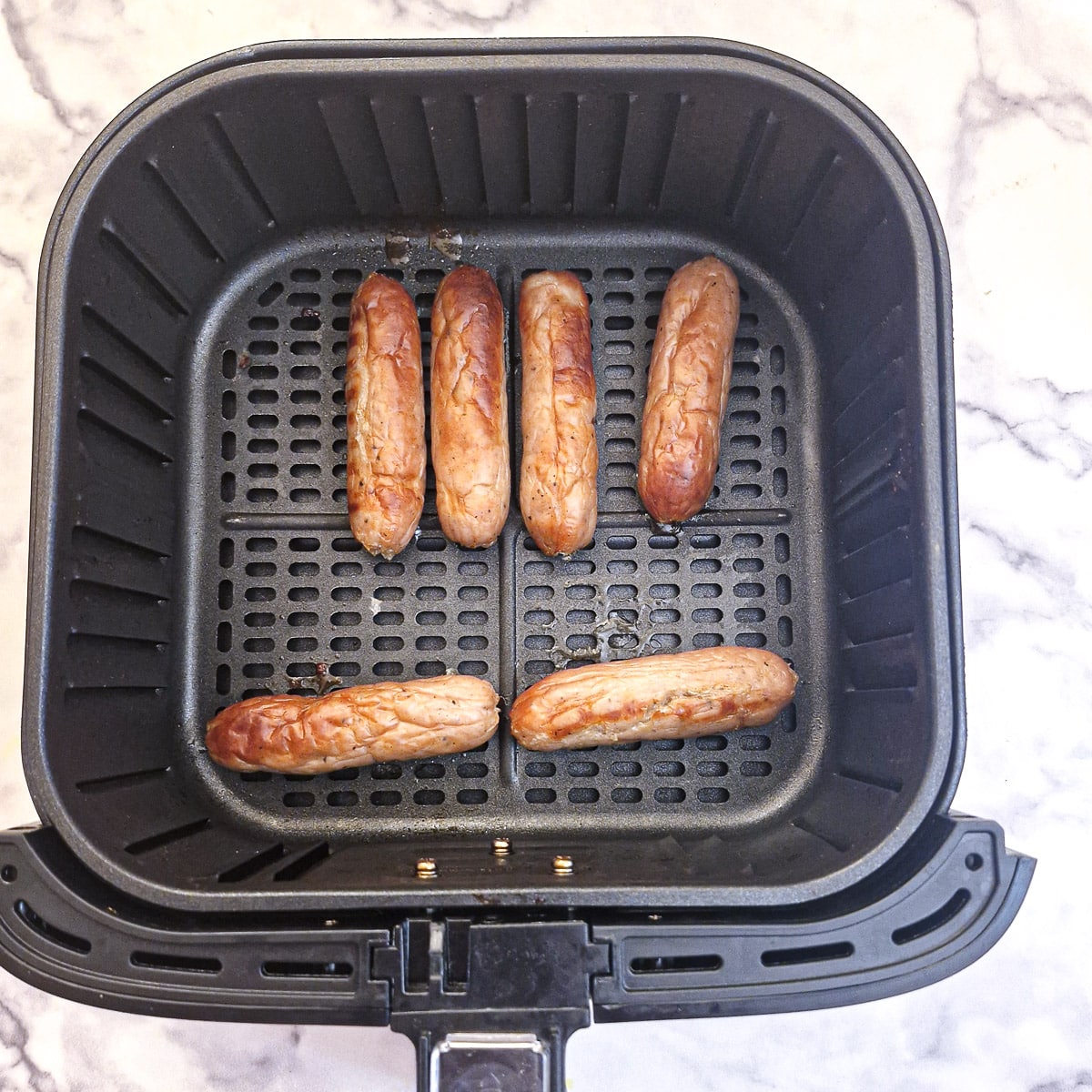 6 cooked sausages in an air fryer basket.