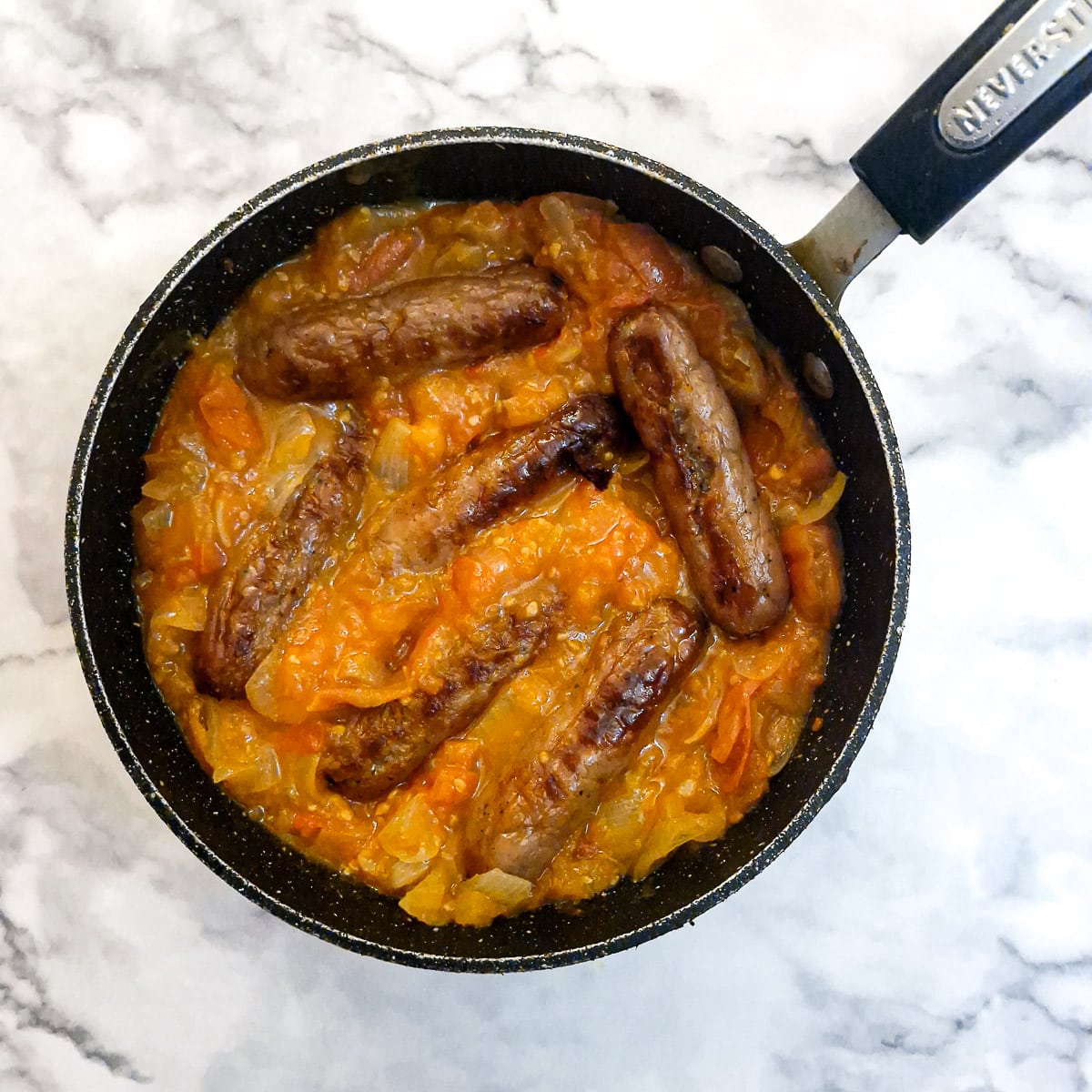 6 sausages arranged in a pan of tomato gravy.
