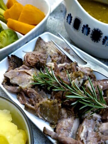 A plate of shredded lamb shoulder with dishes of vegetables and gravy.