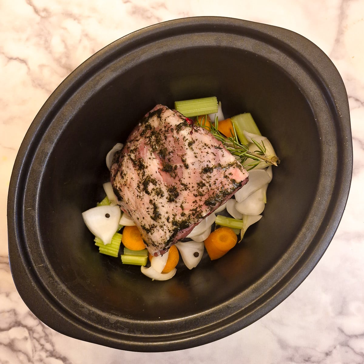 A piece of lamb shoulder covered in mint sauce on the vegetables in a slow cooker.