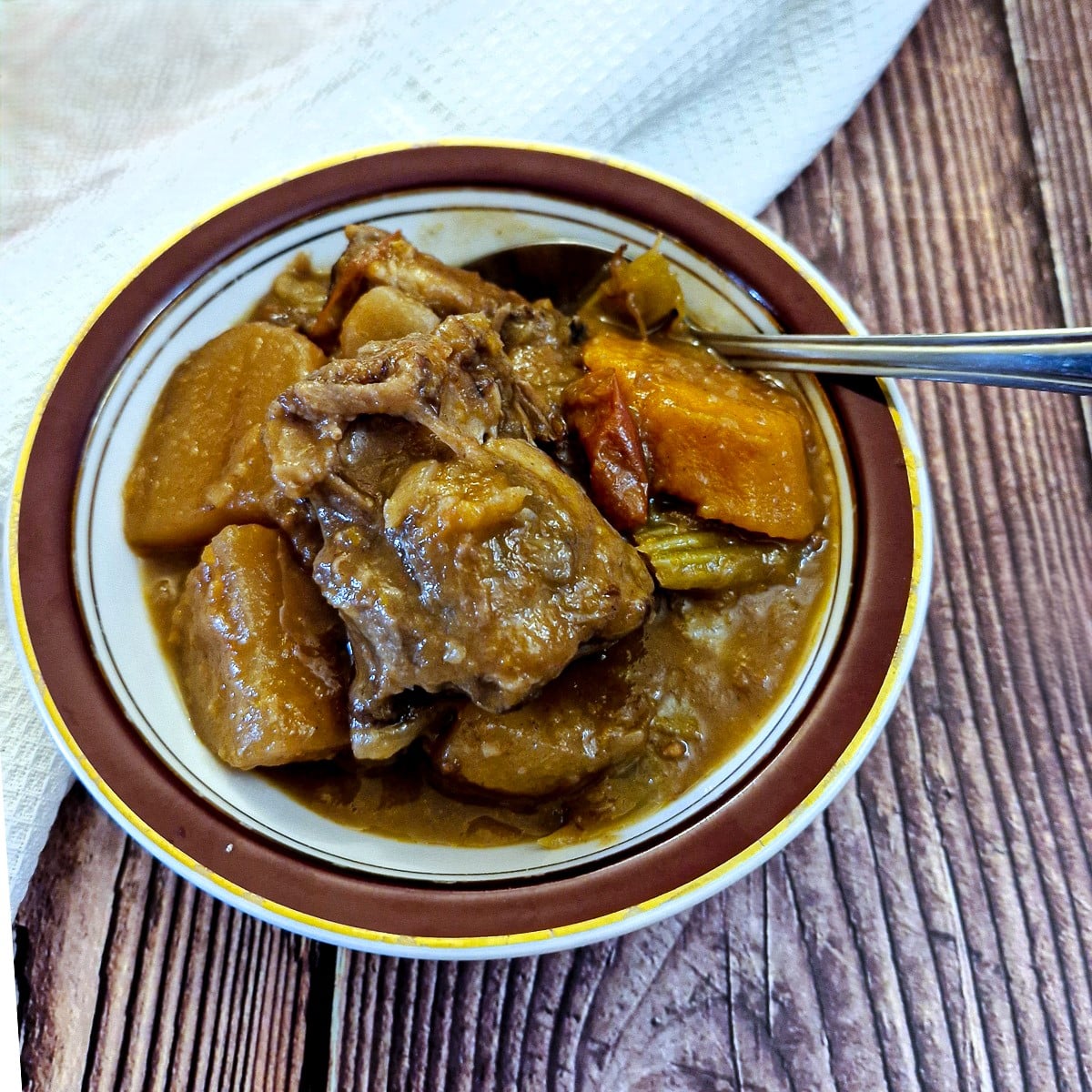 A small dish of oxtail stew with a spoon.