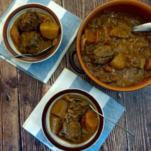 A dish of oxtail stew on a table next to 2 smaller dishes of oxtail stew.