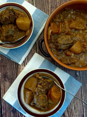 A dish of oxtail stew on a table next to 2 smaller dishes of oxtail stew.