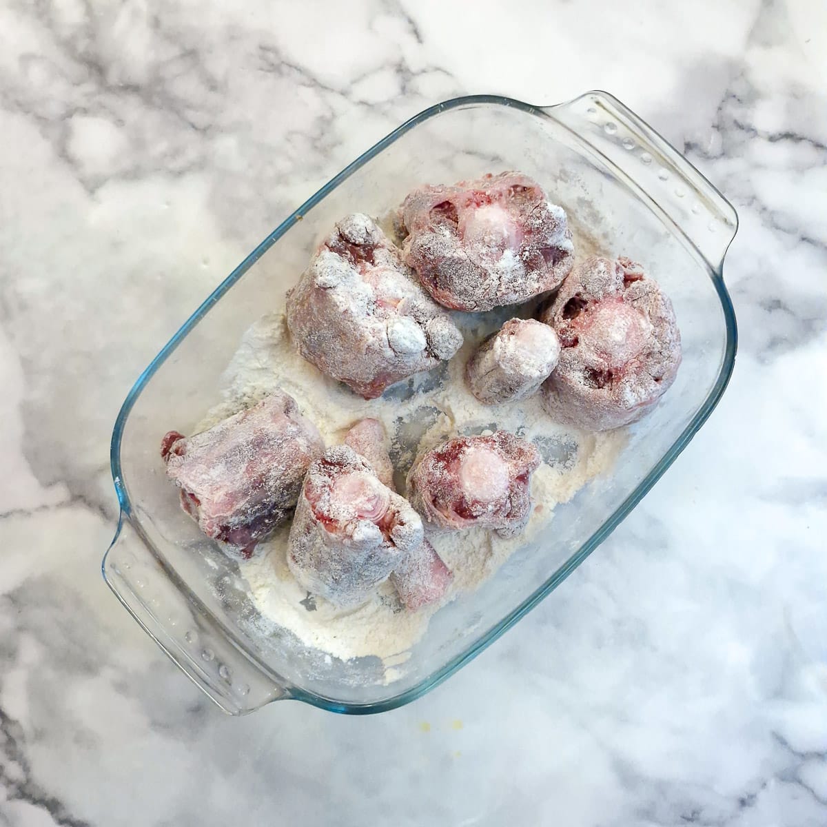 Oxtail bones coated in flour in a glass dish.