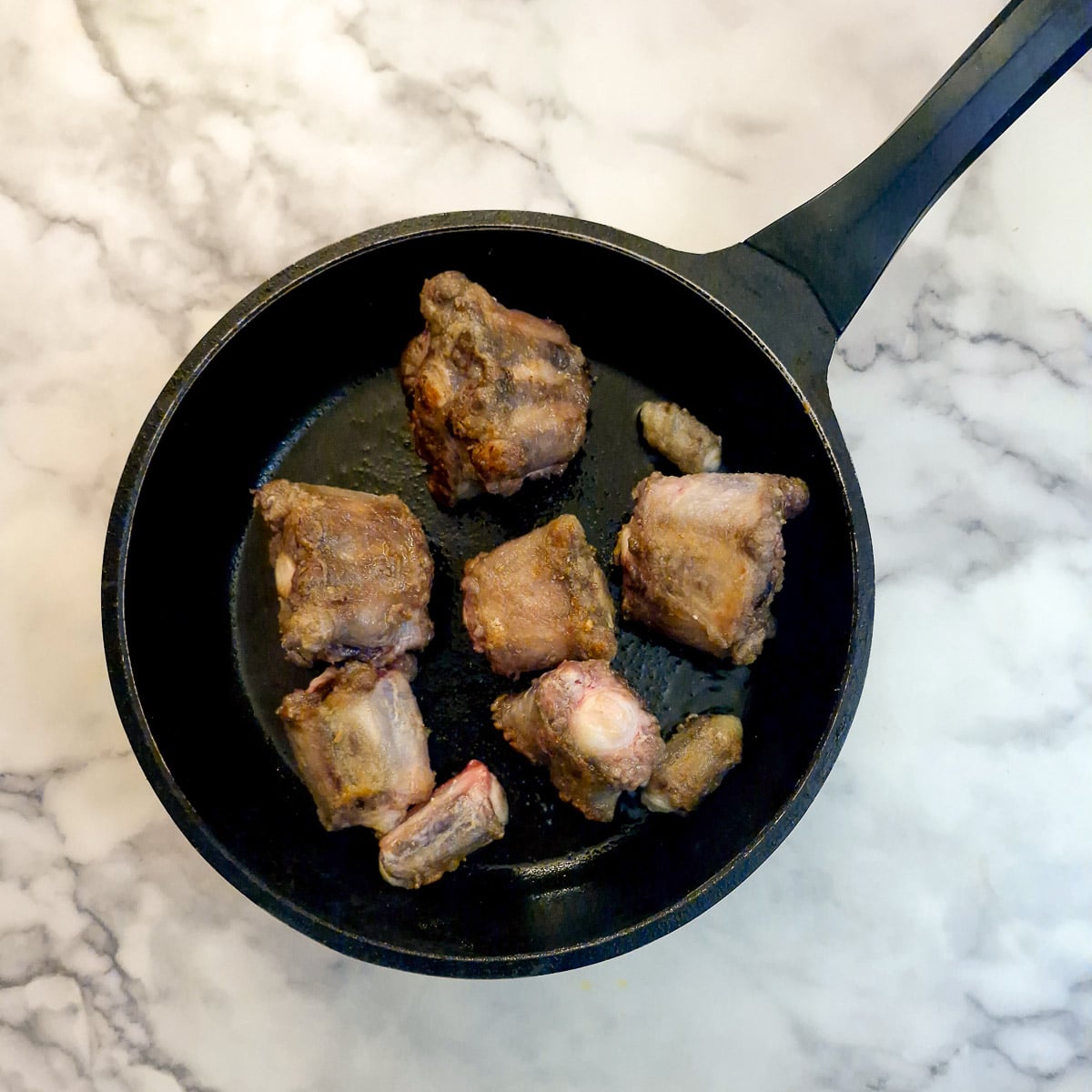 Oxtail bones browning in a frying pan.